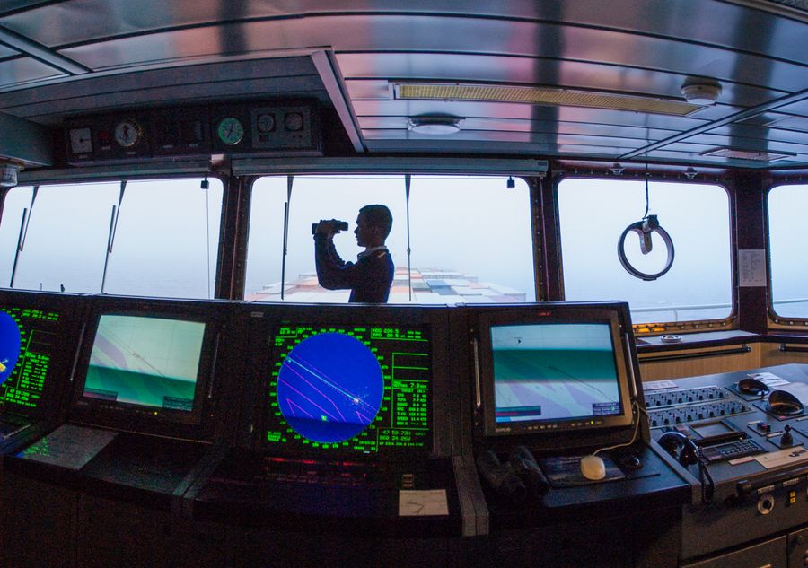 Navigating officer keeping lookout on a ship's bridge beside radar displays